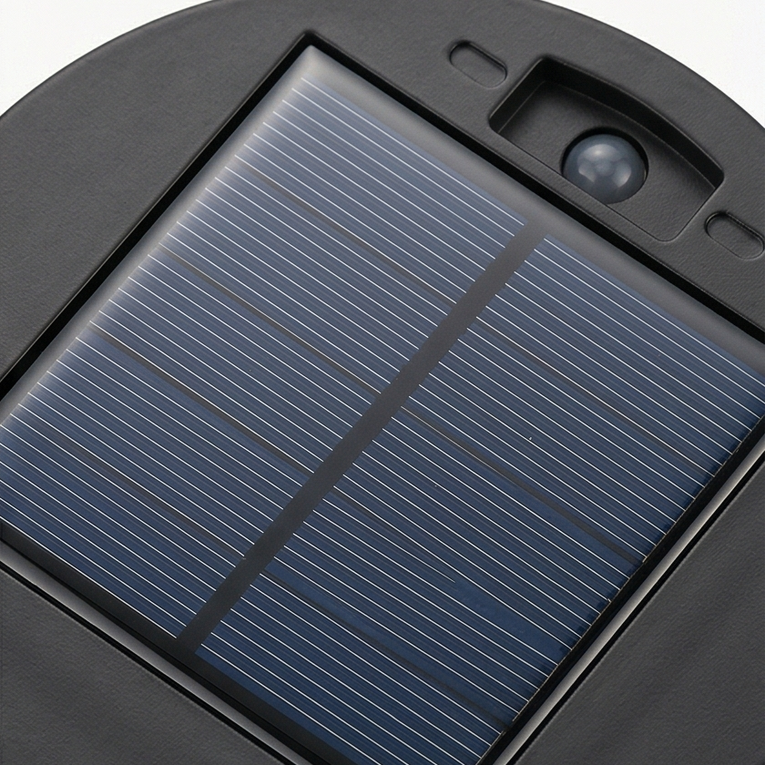 Black cylindrical solar lantern projecting warm patterned light on a wall and patio