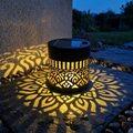 Black cylindrical solar lantern projecting warm patterned light on a wall and patio